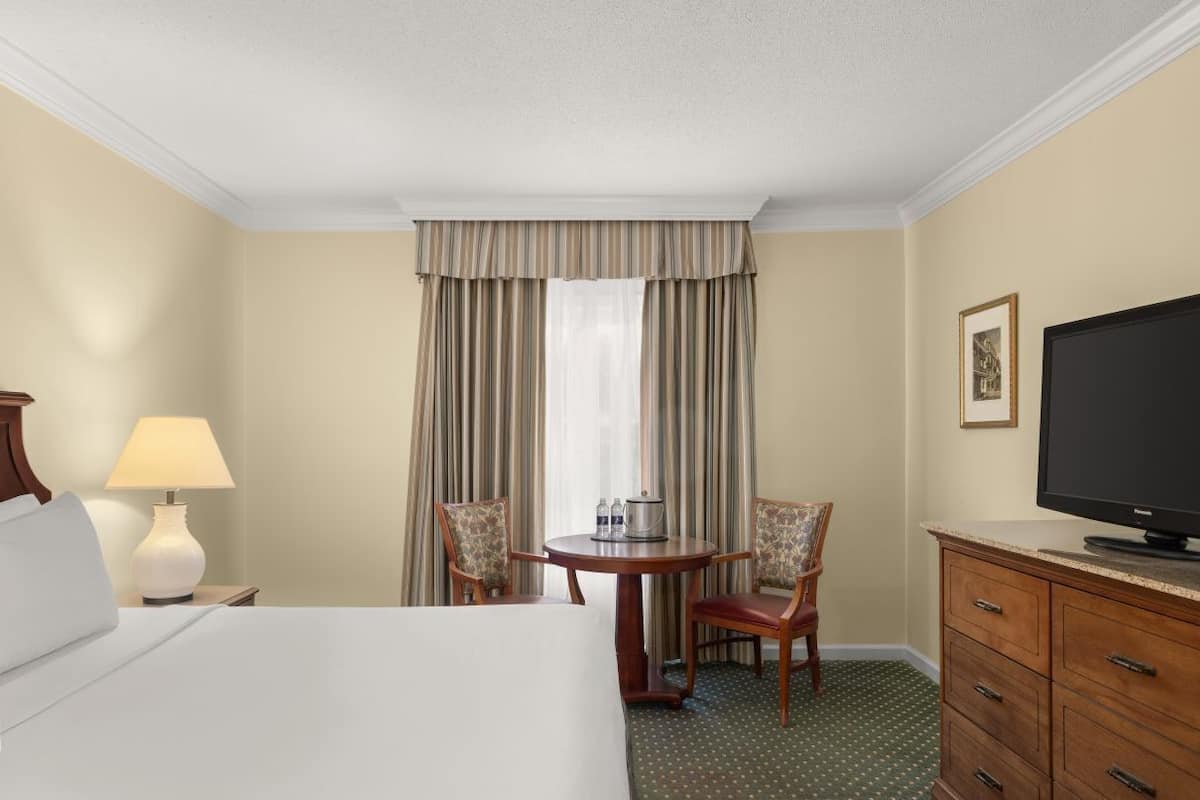 Una habitación de hotel con una cama, un escritorio con lámpara, televisión y una silla.