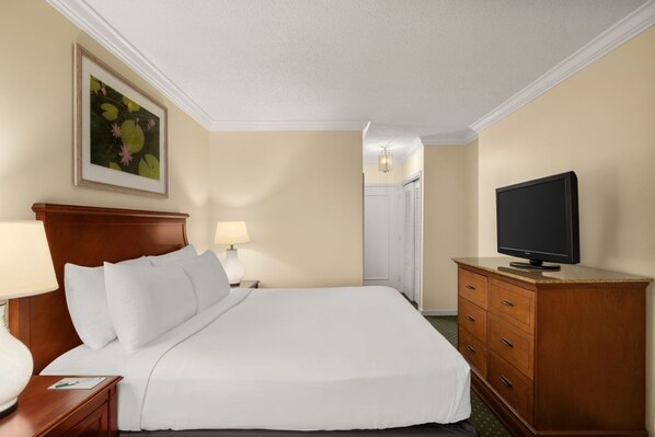 A hotel room with a large bed, a wooden dresser, a television, and a framed artwork on the wall.