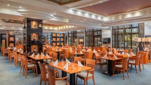 Un restaurante espacioso con numerosas mesas y sillas, ventanas amplias y un diseño moderno en el techo.