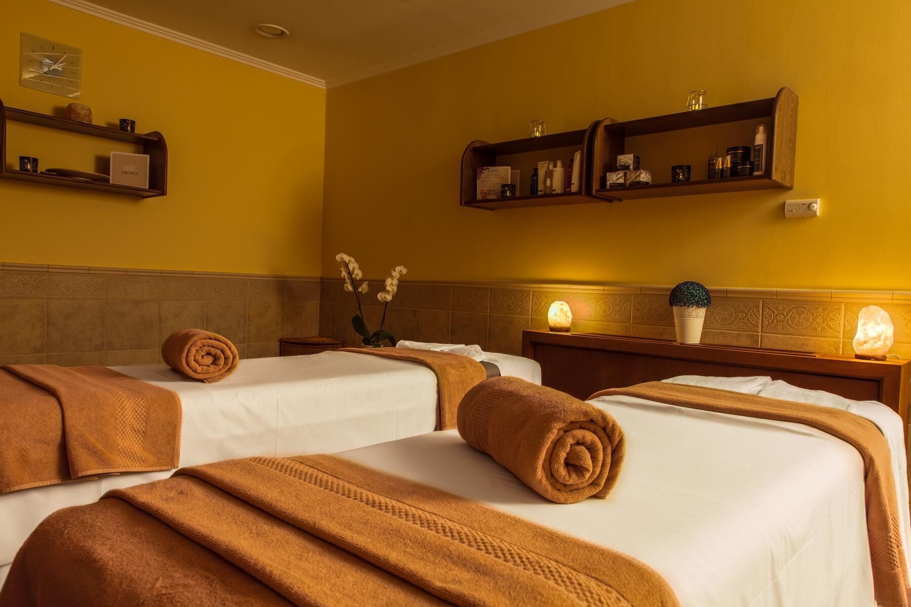 Hotelkamer met twee bedden, elk voorzien van een opgerolde handdoek, een nachtlampje en een plank met toiletartikelen.