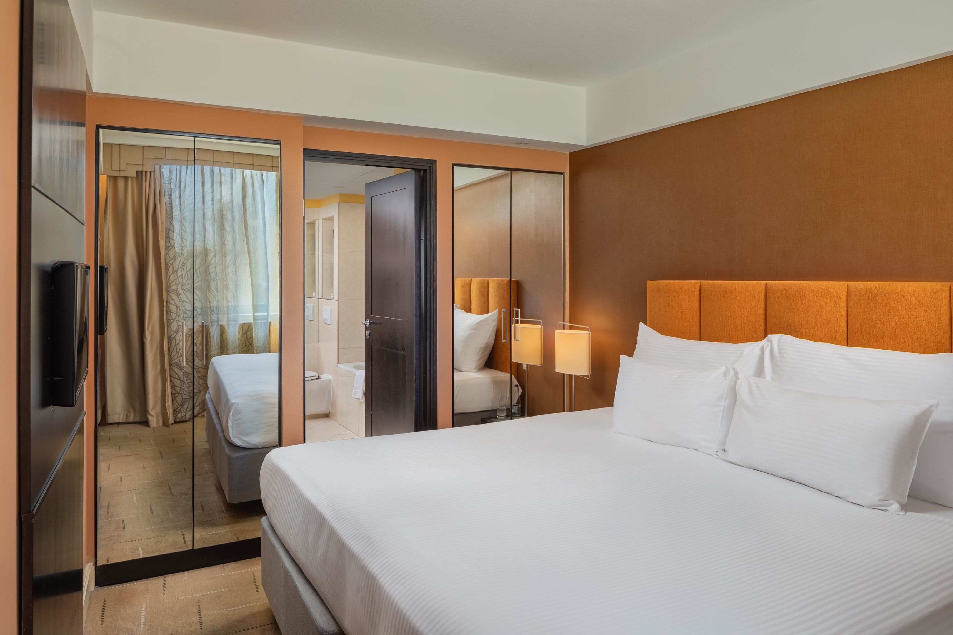 A hotel room with a large bed, a mirror, a wardrobe, and a television.
