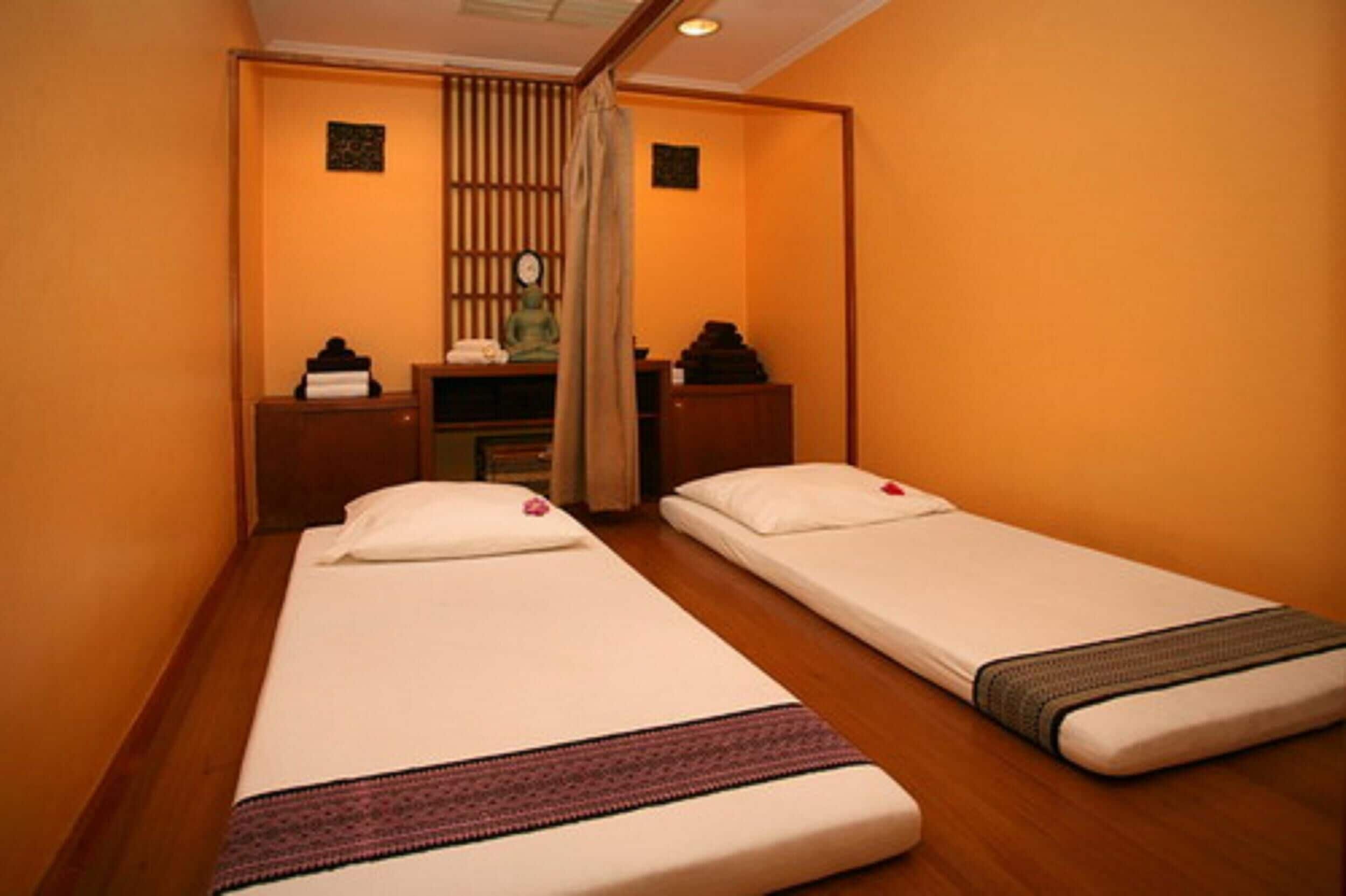 A room with two single beds, wooden flooring, a small desk with a chair, and a wall-mounted clock.