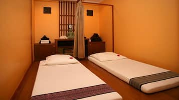 A room with two single beds, wooden flooring, a small desk with a chair, and a wall-mounted clock.