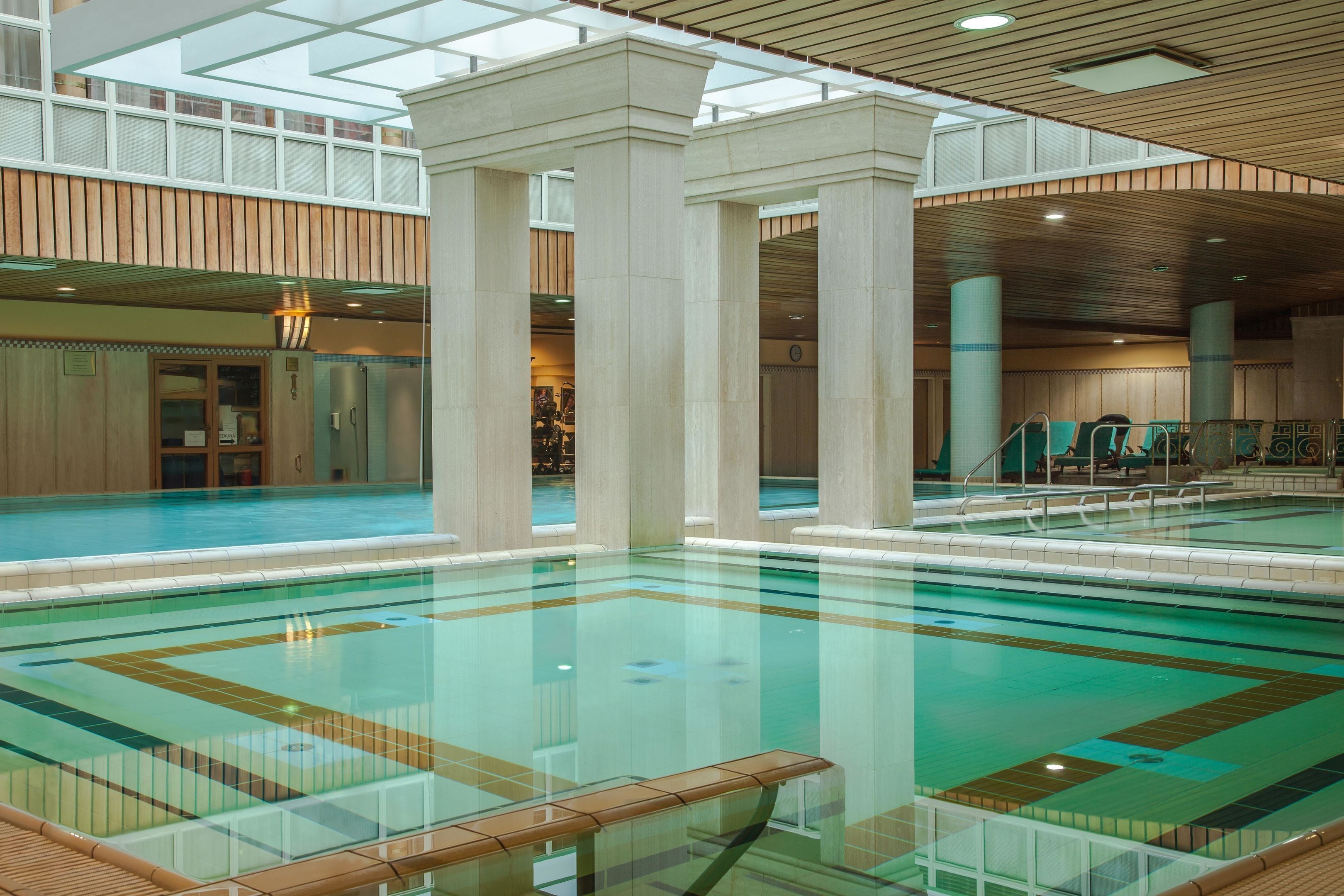 An indoor swimming pool with clear water, surrounded by columns, and a wooden ceiling.
