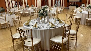 Un salón de banquetes con mesas redondas, sillas doradas, manteles blancos y centros de mesa florales.