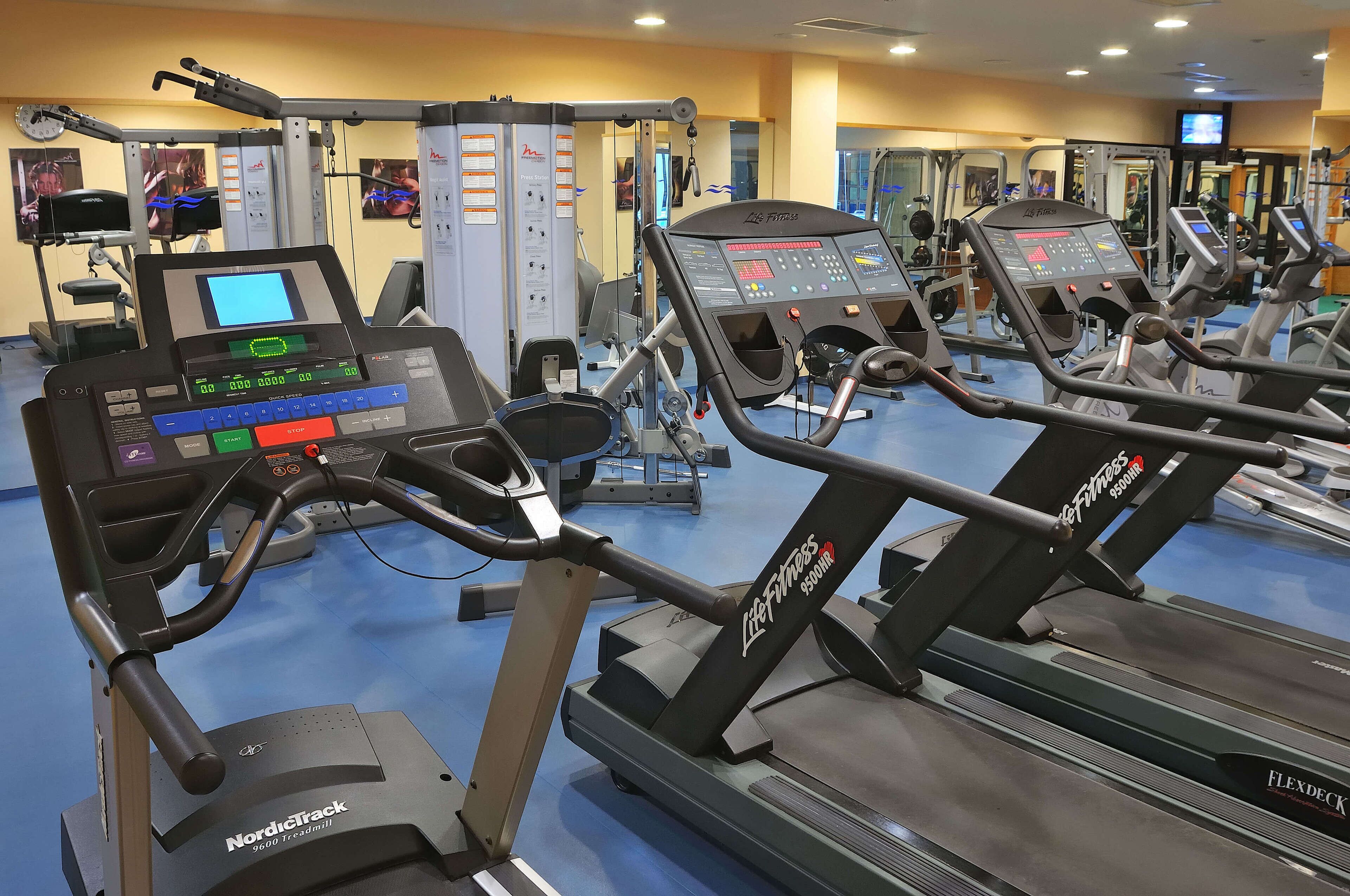 Une salle de sport équipée de tapis de course, d’appareils de musculation et d’un écran numérique.