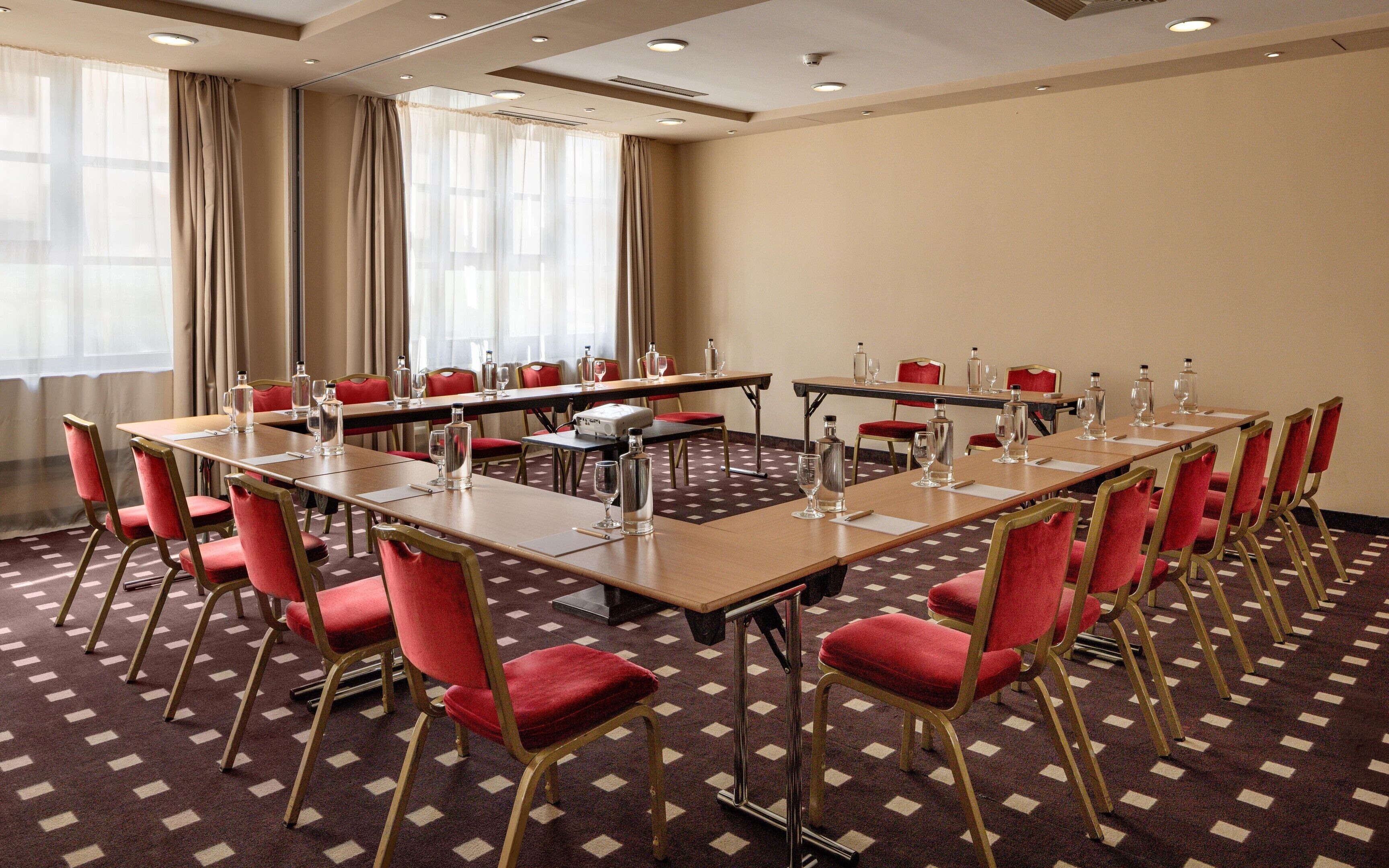Uma sala de conferência com várias mesas e cadeiras, equipada com garrafas de água e copos.