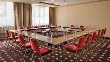 Uma sala de conferência com várias mesas e cadeiras, equipada com garrafas de água e copos.