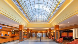 Un hall de hotel con techo de cristal, mostrador de recepción, zona de estar y ascensores.