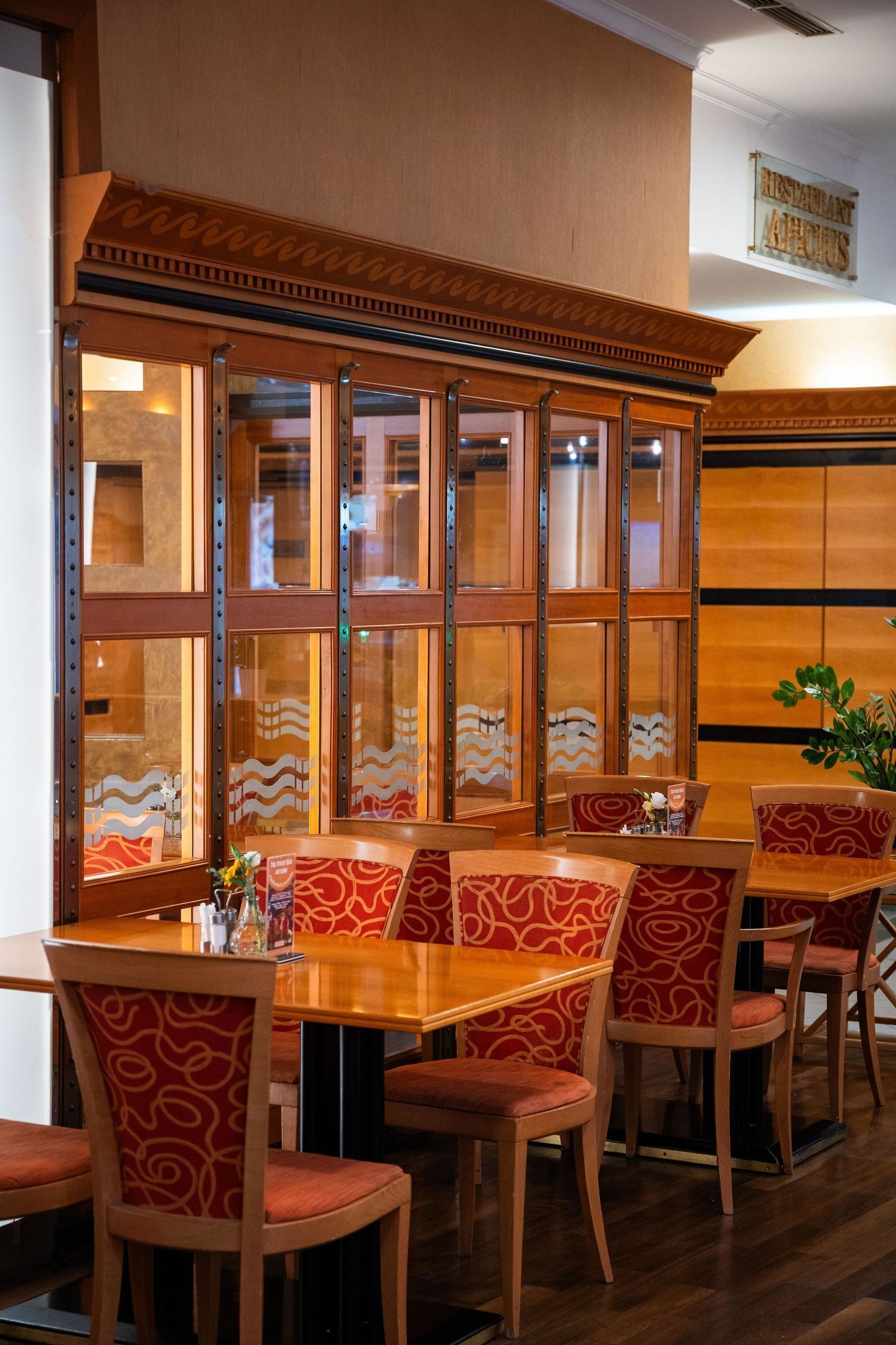 A restaurant interior with wooden tables and chairs, a decorative wall with a wavy pattern, and a sign above the entrance.