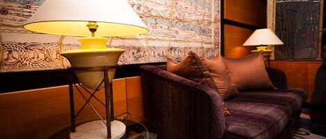 Ein Zimmer mit einem violetten Sofa, einem runden Tisch mit Lampe und einer großen Wand mit Muster.