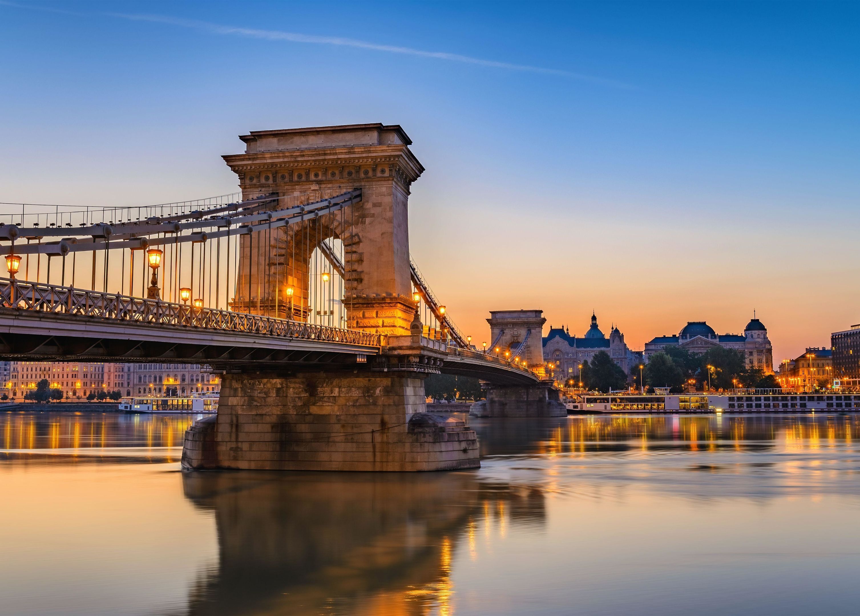 A bridge with a stone tower, a calm river, and buildings in the background.