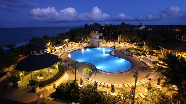 A resort pool area with a gazebo, lounge chairs, and a view of the ocean at dusk. - Disney's Vero Beach Resort (Vero Beach)