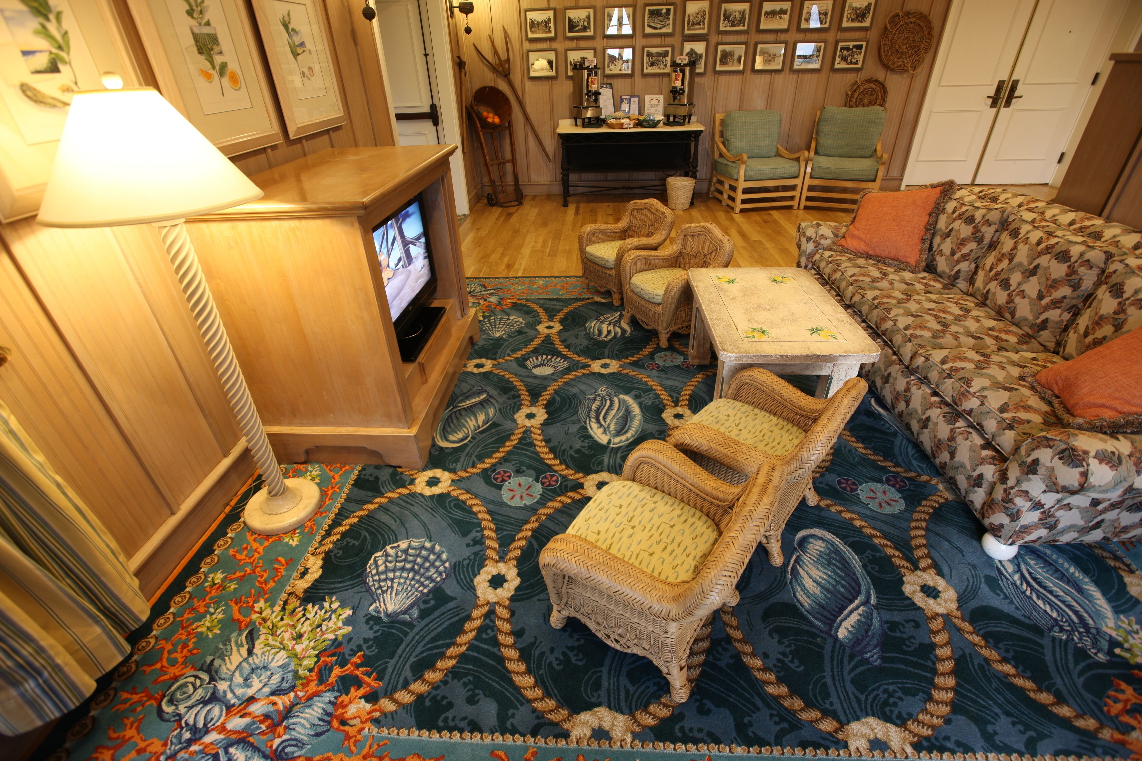A cozy living room with a television, wicker chairs, a patterned rug, and a sofa.