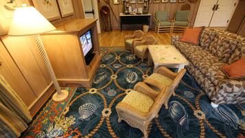 A cozy living room with a television, wicker chairs, a patterned rug, and a sofa.