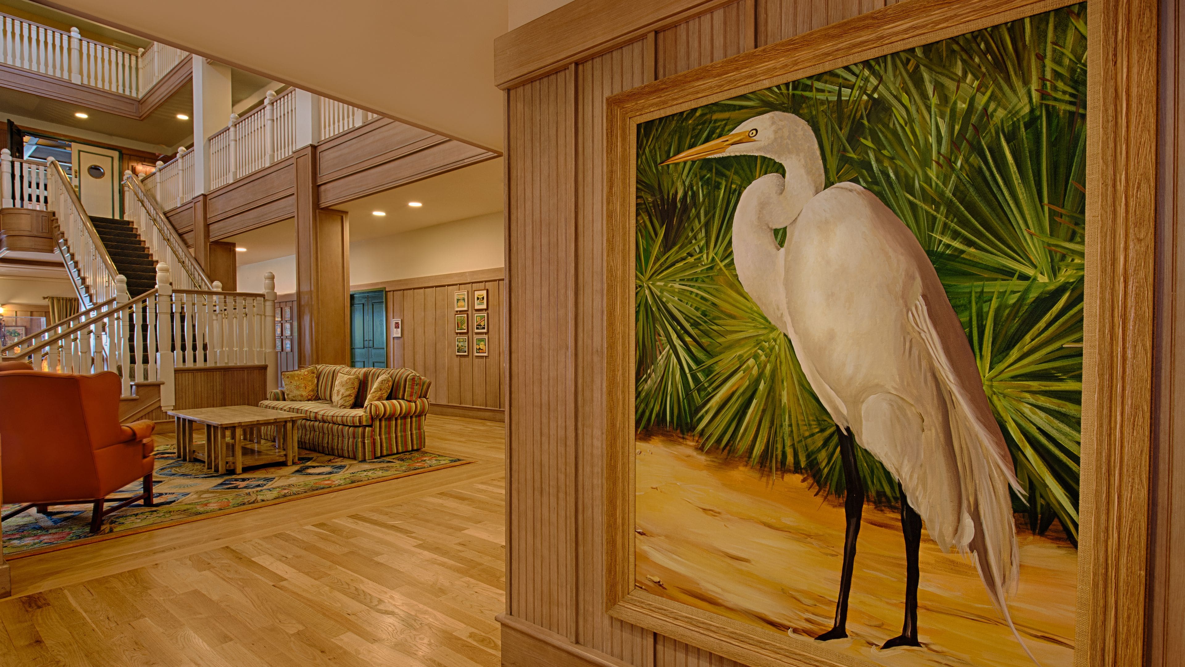 A spacious living area with a wooden floor, a striped sofa, a coffee table, and a framed painting of a white bird.