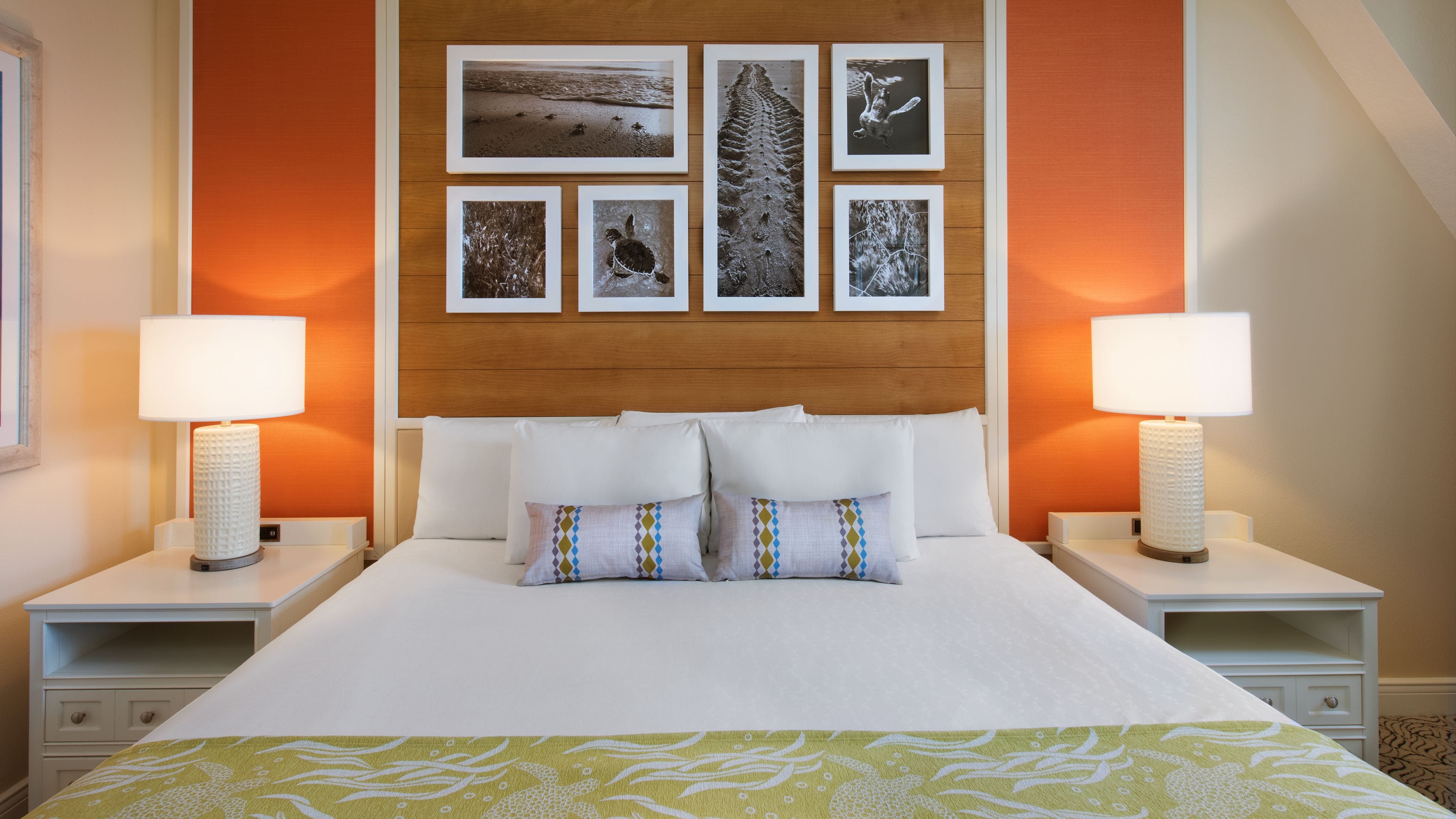 A hotel room with a large bed, two bedside tables with lamps, a wooden headboard, and a wall decorated with framed pictures.