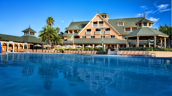 Un resort con una piscina grande, varias zonas de descanso y un edificio de varios pisos con un estilo arquitectónico distintivo.