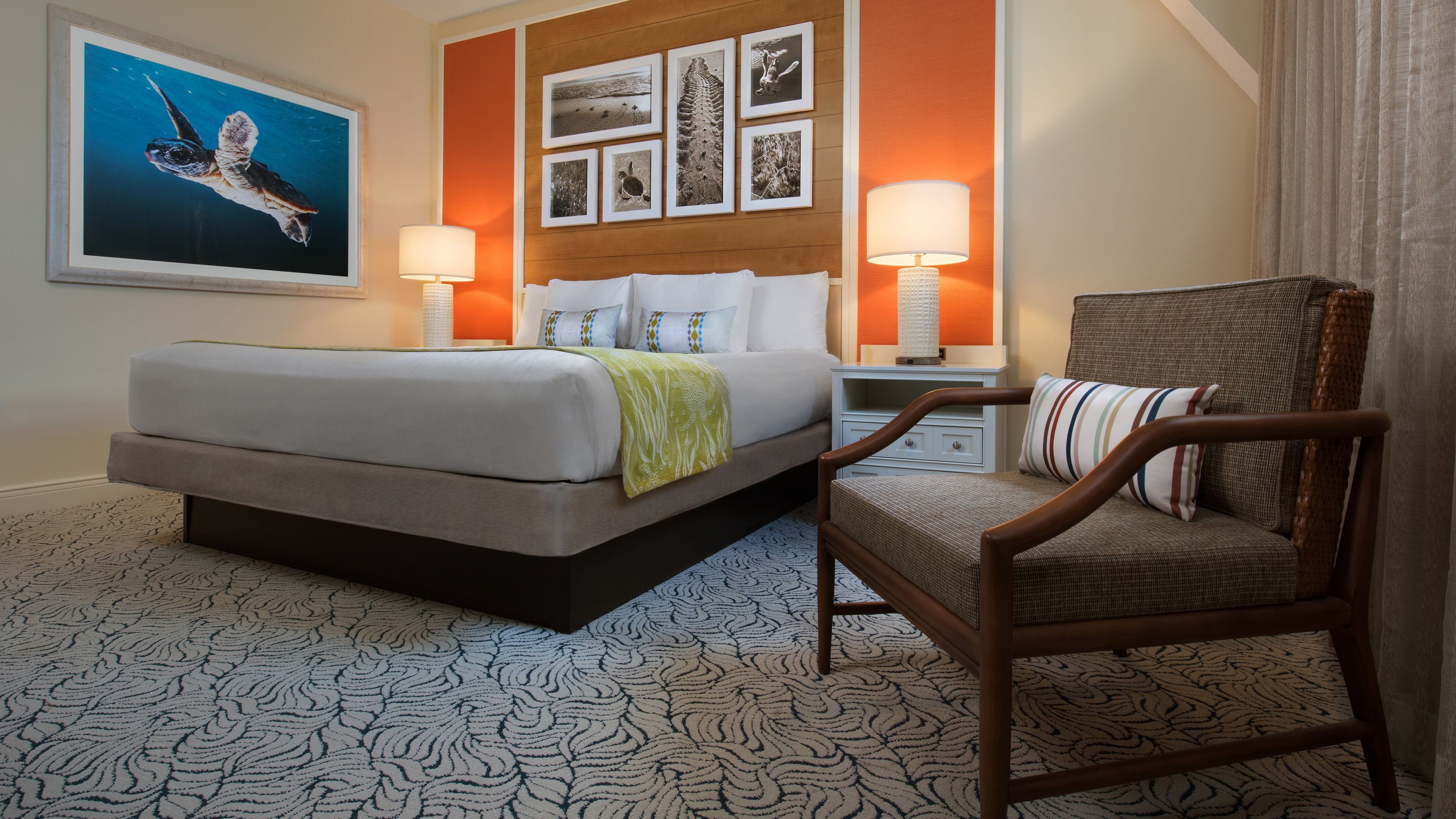 A hotel room with a bed, two bedside lamps, a chair, and a wall with framed pictures.