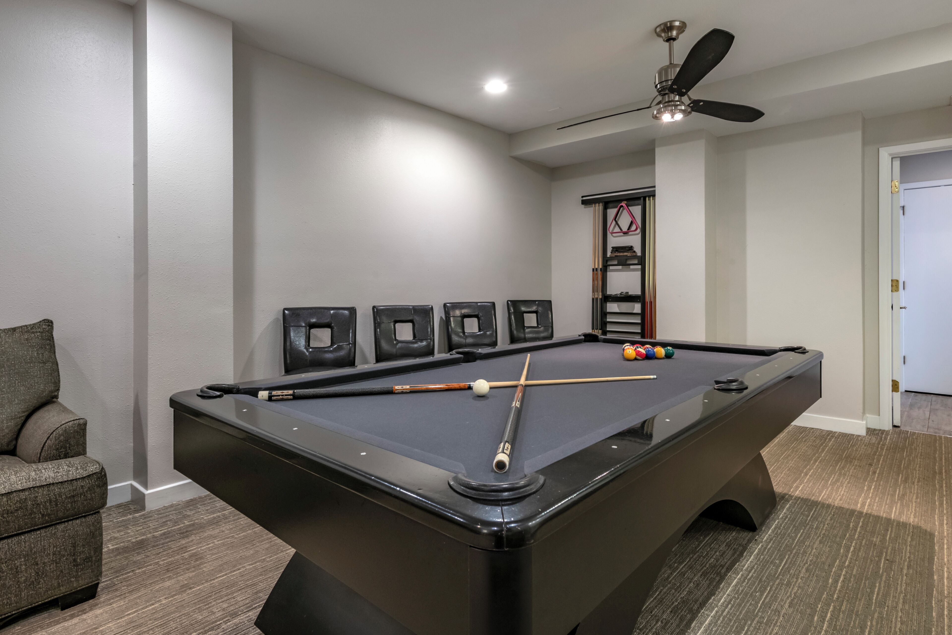 Een pooltafel met een plafondventilator, een biljartkeu en biljartballen.