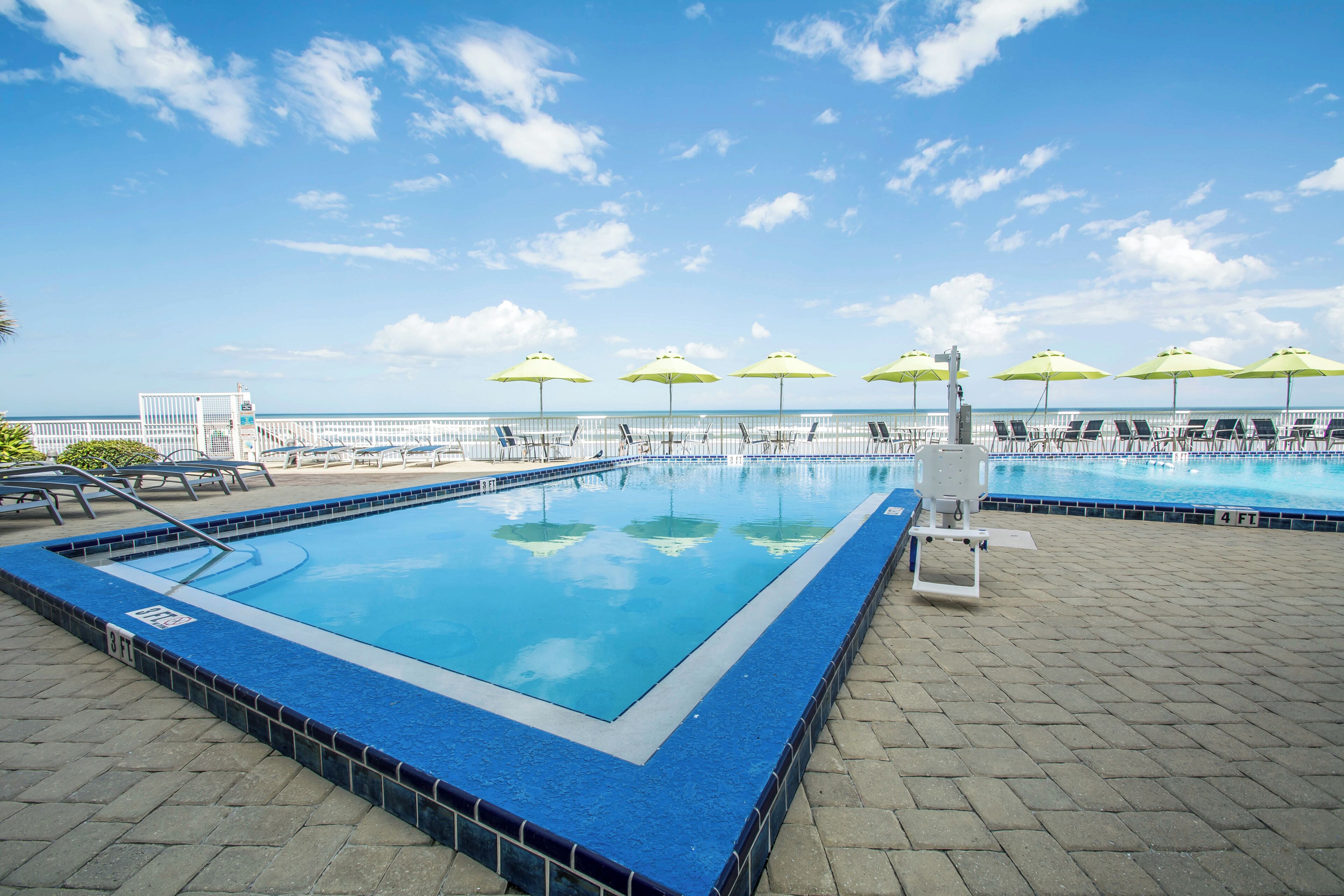 Une piscine dotée de plusieurs couloirs, entourée de chaises longues et de parasols, et offrant une vue sur l’océan.