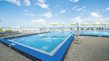 Una piscina con varias pistas, rodeada de tumbonas y sombrillas, y vista al océano.