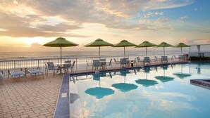 Zona junto a la piscina con sillones y sombrillas, con vista al océano.