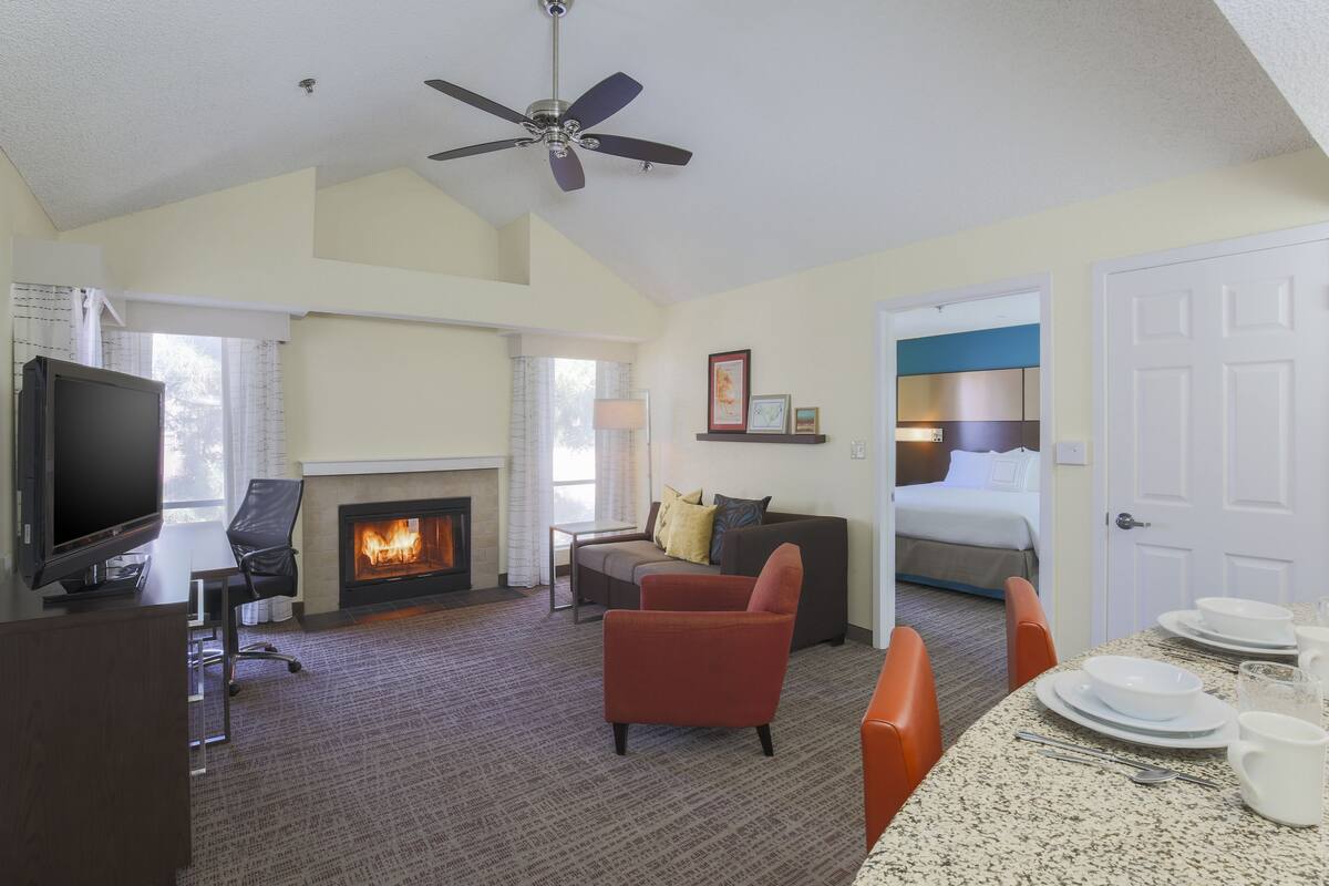A hotel room with a television, fireplace, sofa, armchair, dining table, and a bed.