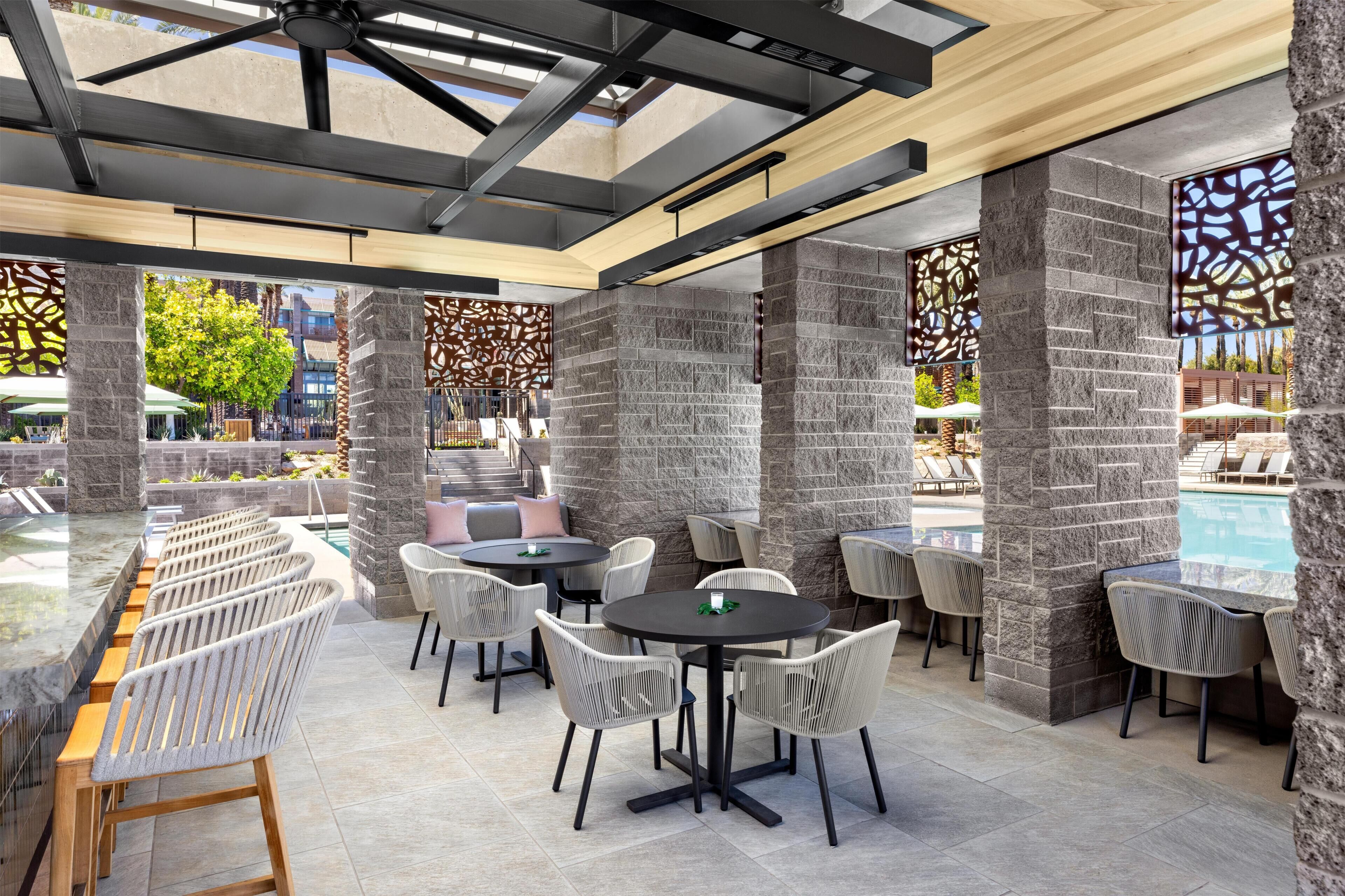 An outdoor dining area with stone pillars, round tables, and wicker chairs.
