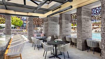 An outdoor dining area with stone pillars, round tables, and wicker chairs.