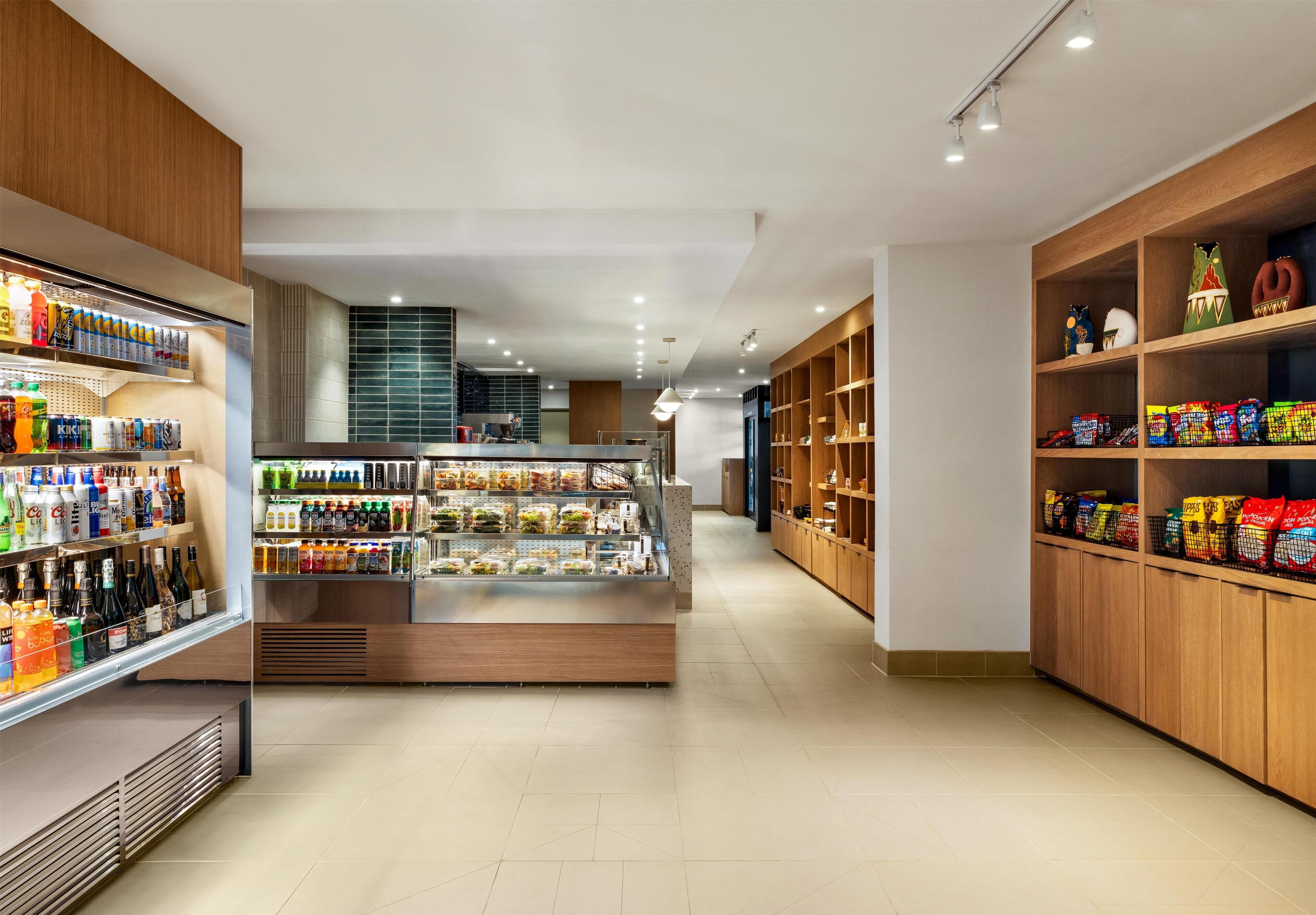 A modern retail space with shelves stocked with beverages and snacks, a refrigerated display case, and wooden shelving units.
