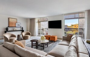 A modern living room with a sofa, armchairs, a coffee table, and a TV mounted on the wall.