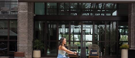 A woman riding a bicycle in front of a building with a modern architectural design, featuring large windows and a decorative facade.
