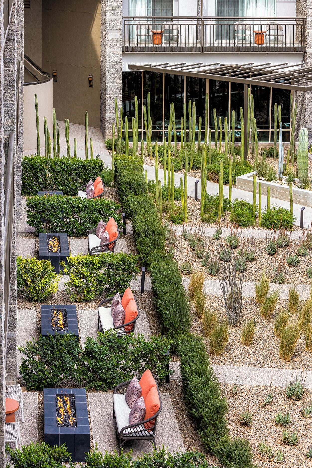 Un área exterior ajardinada con un espacio de descanso que incluye sillas y mesas, rodeada de diversas plantas y cactus.