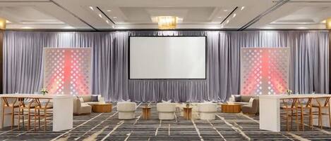 Une salle de conférence dotée d’un grand écran, de rideaux gris et d’une moquette à motifs.