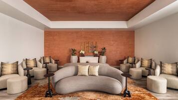 A modern bedroom with a curved bed, multiple seating areas, and a decorative wall piece.