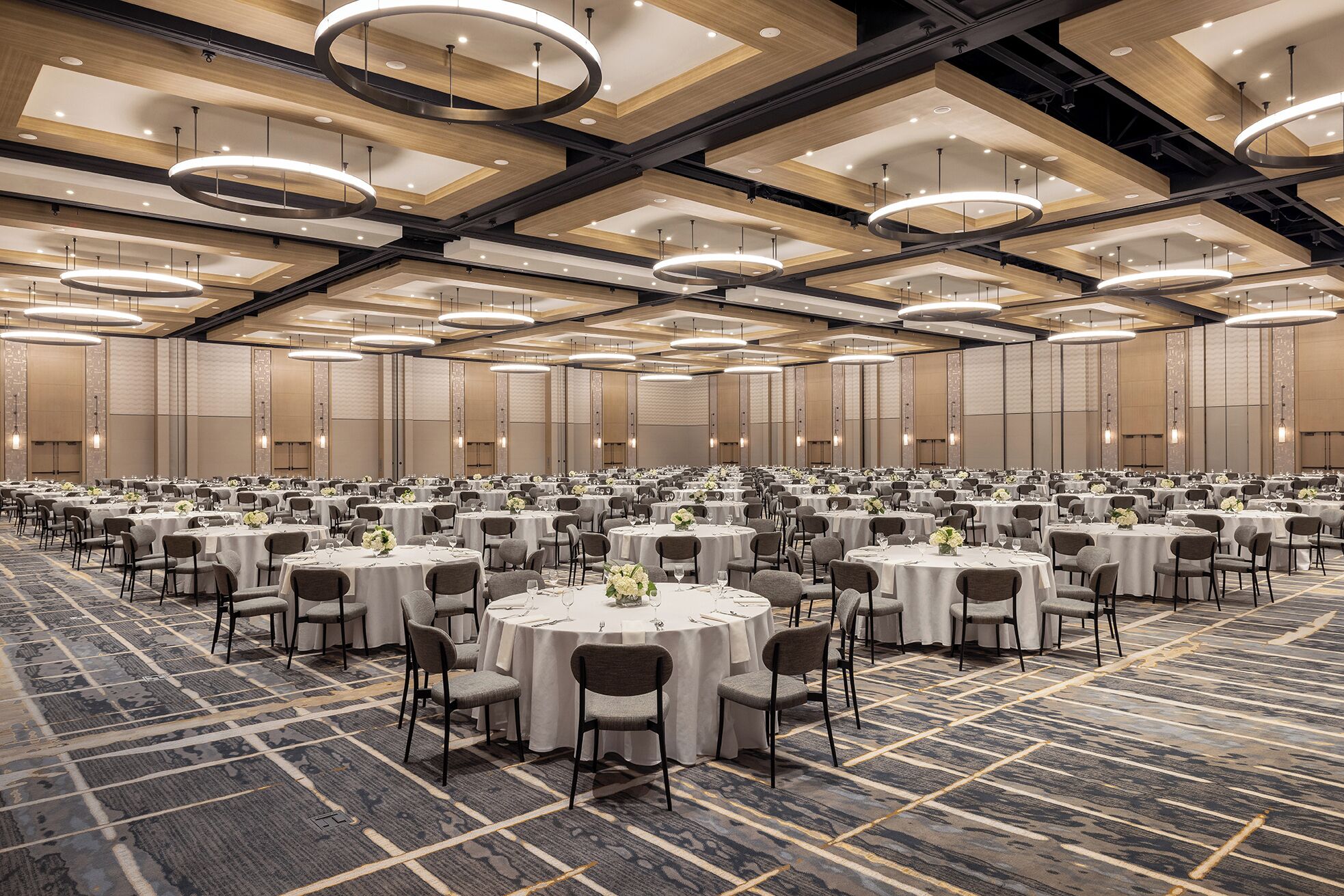 Une grande salle de banquet avec des tables rondes, des chaises et des luminaires modernes.