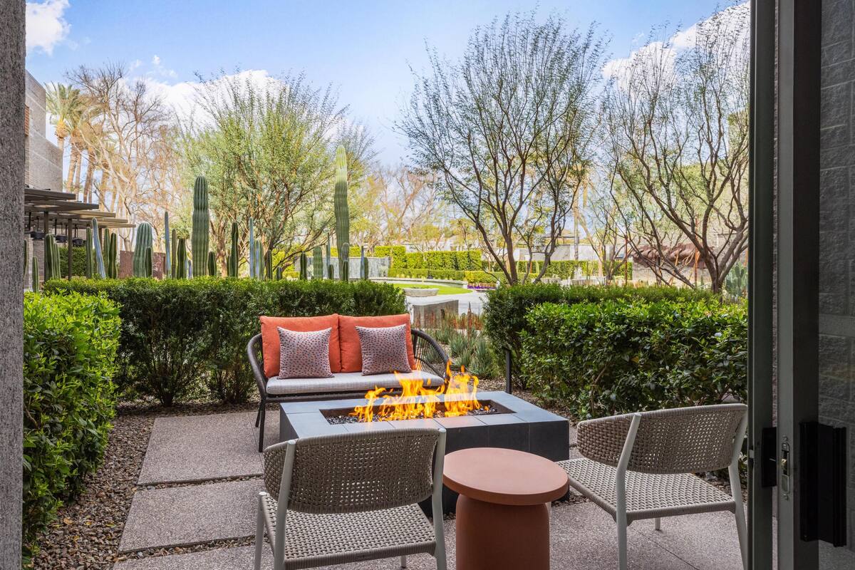 An outdoor patio with a fire pit, wicker furniture, and a view of a landscaped garden with cacti and trees.
