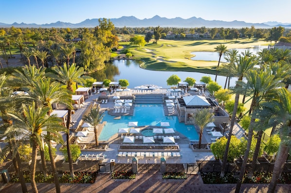 A resort with a swimming pool, palm trees, and a golf course in the background.