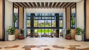 Un hall d’entrée spacieux donnant sur un terrain de golf, agrémenté de grands pots de plantes et doté d’un sol à motifs.