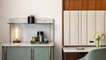 Cozinha moderna com bancada de mármore, cafeteira e um vaso com flores sobre uma mesa lateral.