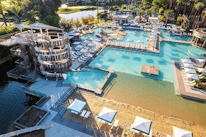 A large, multi-level swimming pool with various sections and lounge areas, surrounded by palm trees and a golf course in the background. - Grand Hyatt Scottsdale Resort (Scottsdale)