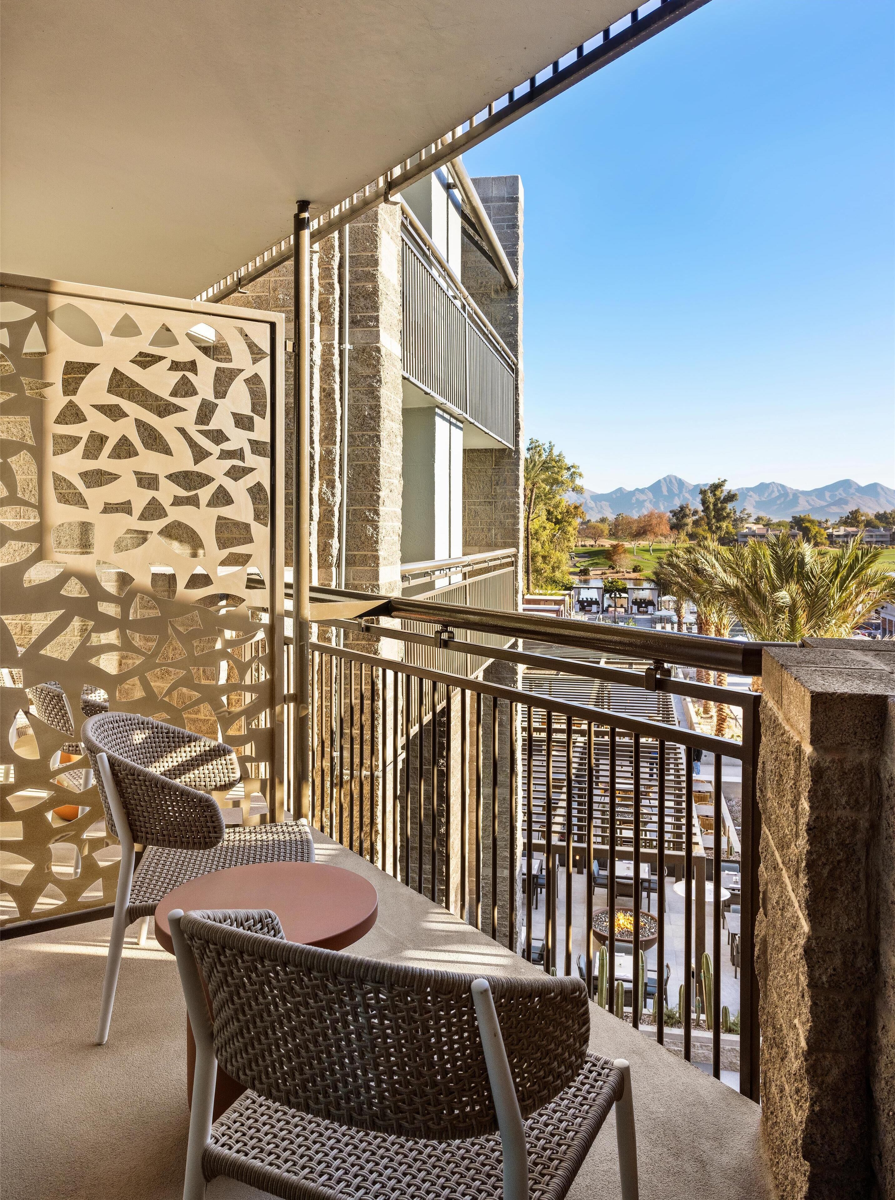 A balcony with wicker chairs, a round table, and a view of mountains.