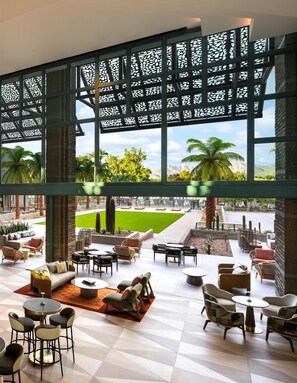 A spacious outdoor lounge area with multiple seating arrangements, a view of a green lawn, and a mountainous landscape.