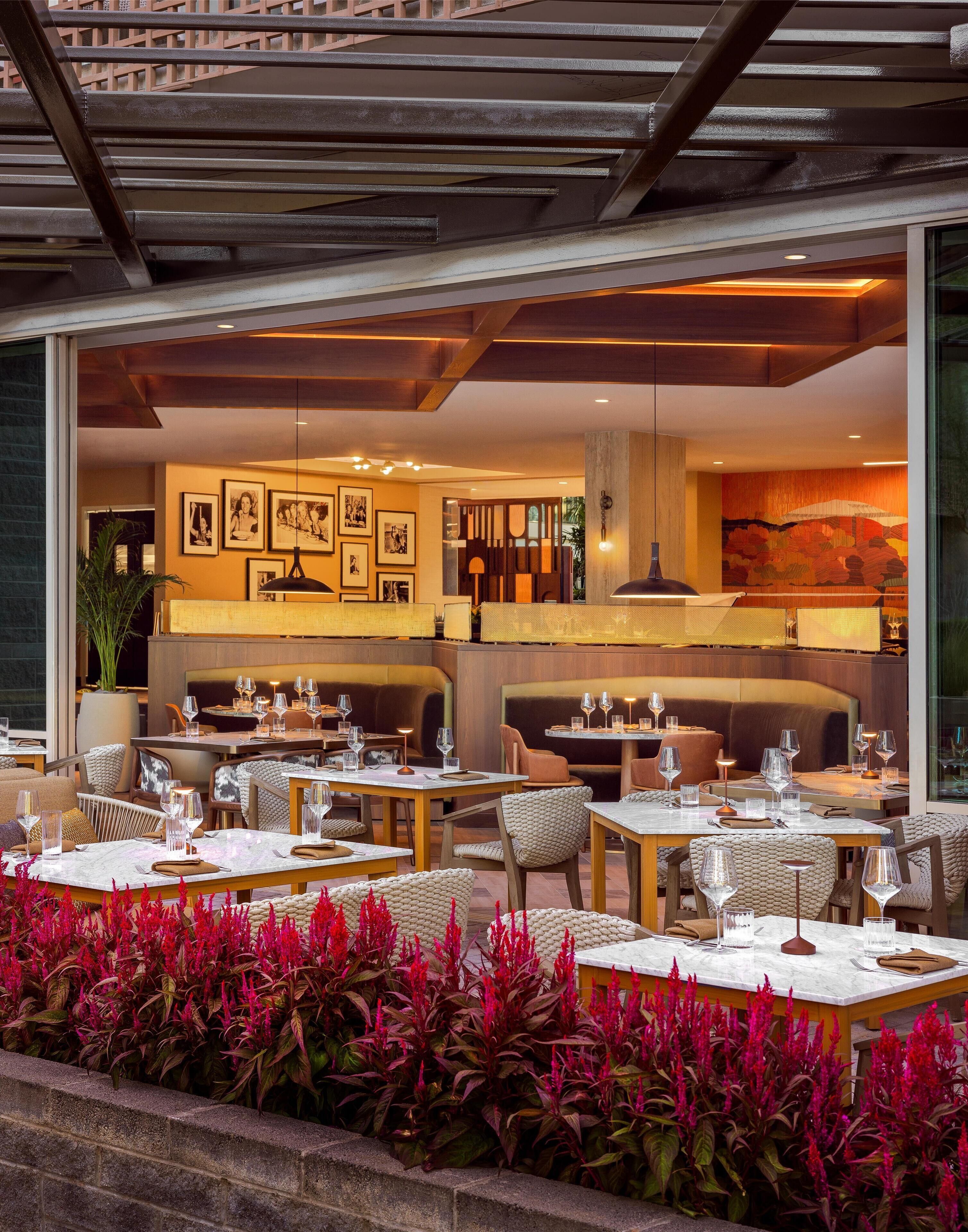 An outdoor dining area with tables and chairs, a bar area with seating, and a view of the interior dining space.