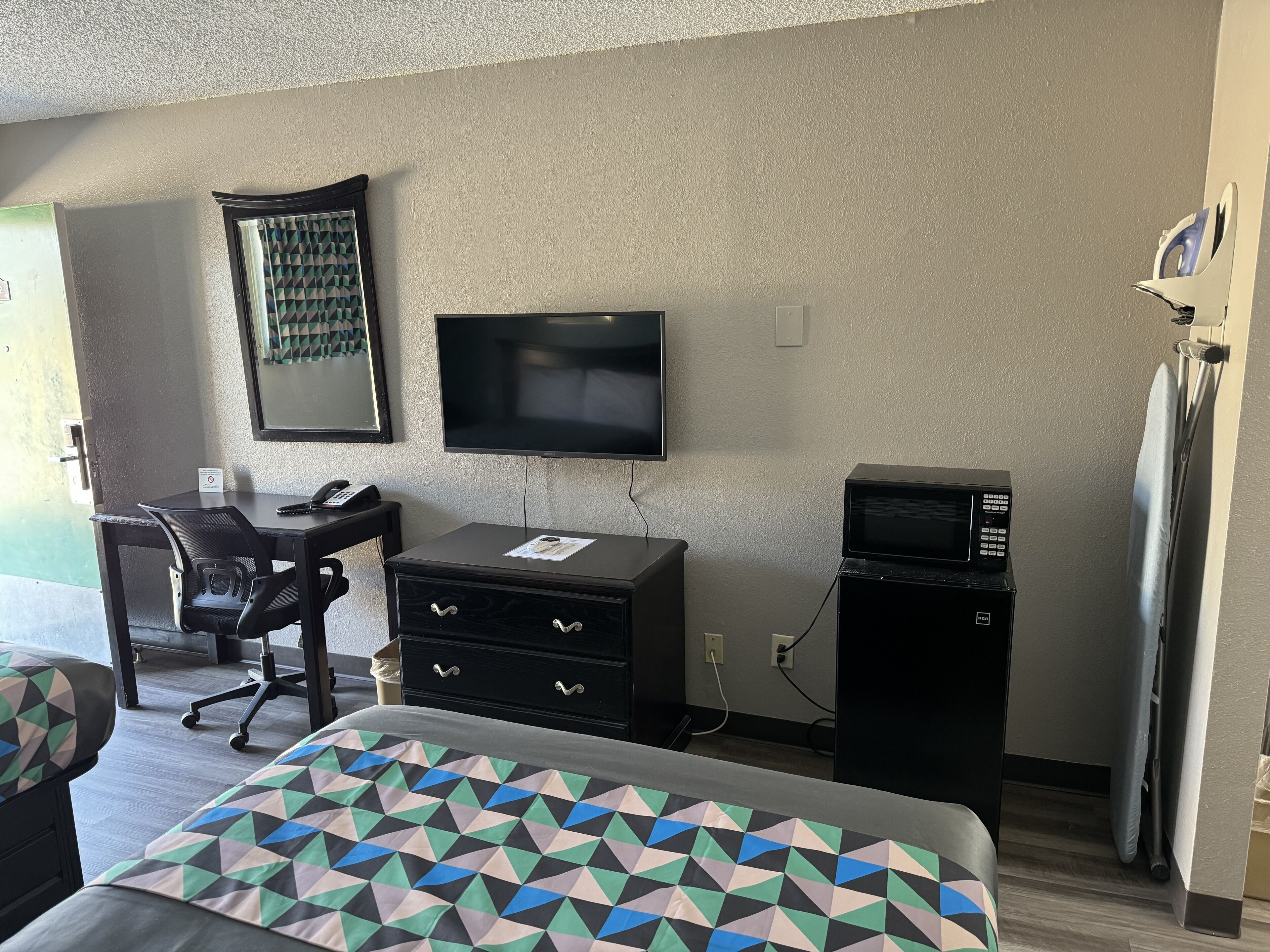 A hotel room with a bed, a desk with a chair, a television, a microwave, and a small refrigerator.