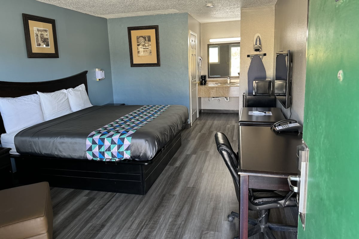 A hotel room with a bed, a desk, a chair, a microwave, and a green wall.