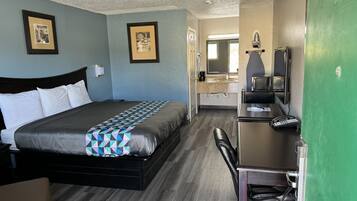 A hotel room with a bed, a desk, a chair, a microwave, and a green wall.