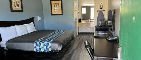 Habitación de hotel con una cama, un escritorio, una silla, un microondas y una pared verde.