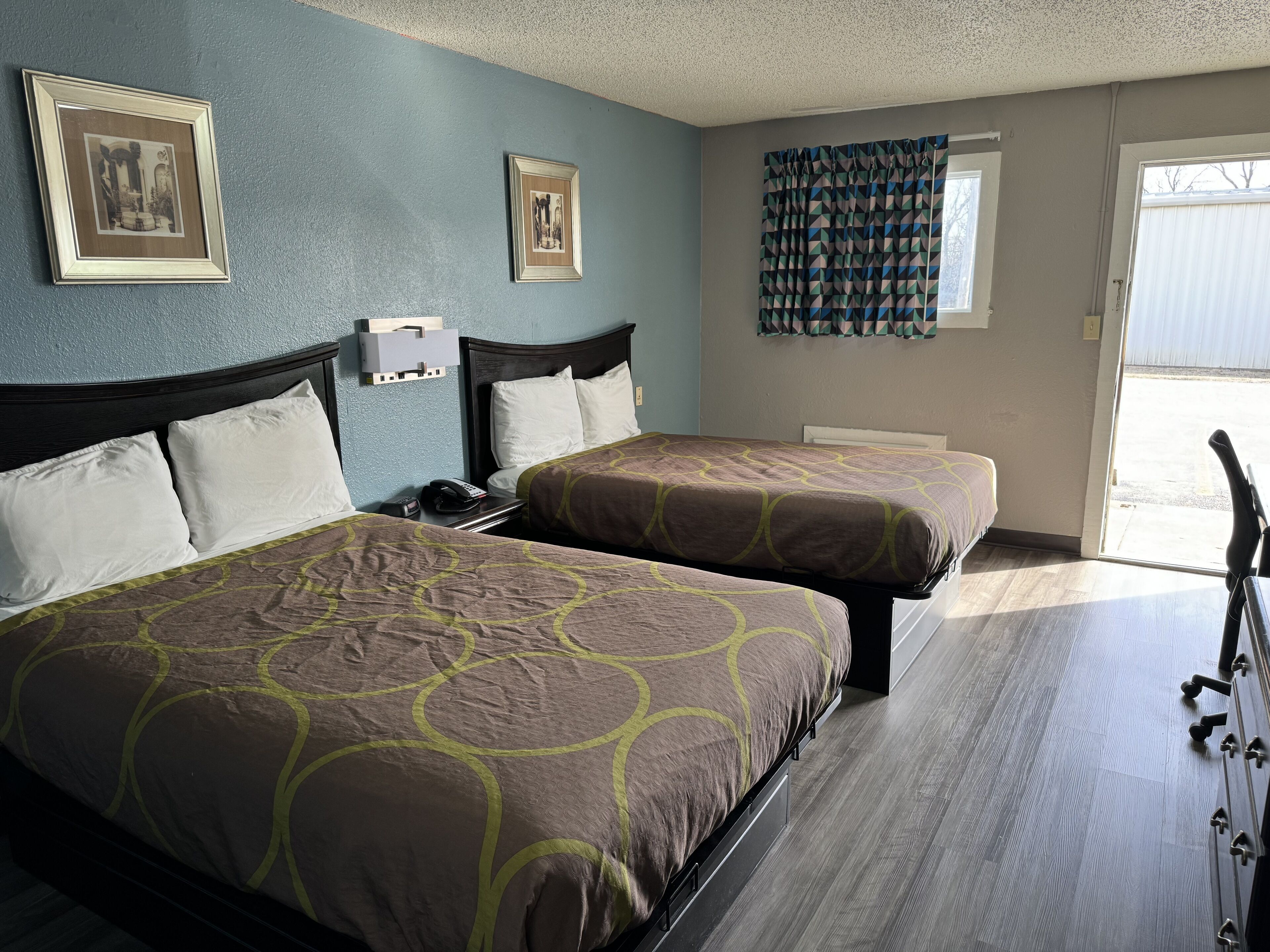 A hotel room with two beds, a nightstand, a telephone, and a window with curtains.